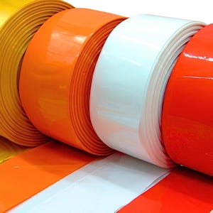 Può includere: Quattro grandi rotoli di nastro adesivo lucido disposti fianco a fianco. I colori da sinistra a destra sono giallo, arancione, bianco e rosso brillante. Ogni rotolo è avvolto strettamente, mostrando una superficie liscia e riflettente.
