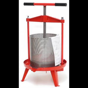 Puede incluir: Una prensa de frutas roja con un mecanismo de tornillo central con mango horizontal, una cesta perforada de acero inoxidable y una bolsa de filtro de malla blanca. La estructura se apoya en tres patas rojas y una base circular.