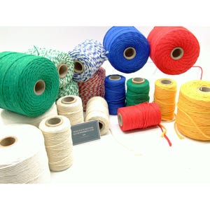 May include: A collection of various spools of twine in solid colours including green, blue, red, yellow, and off-white, alongside multi-coloured striped twine. A small rectangular sign with the text MANUFACTURED FOR ALCOVERMBREW.COM is visible.