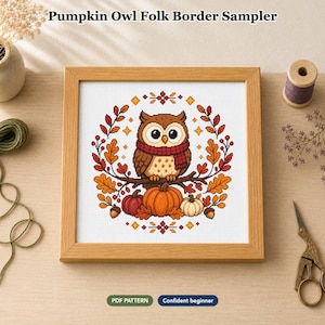 Op de afbeelding: Een vierkante houten lijst met een kruissteekpatroon genaamd Pumpkin Owl Folk Border Sampler. Het ontwerp toont een bruine uil met een rode sjaal op een tak, omringd door oranje pompoenen, eikels en herfstbladeren.