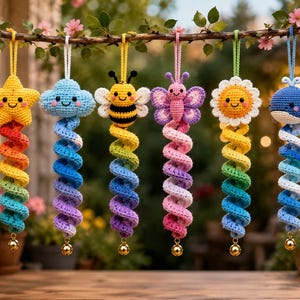May include: Six hanging crochet ornaments featuring a yellow star, blue cloud, yellow and black bee, purple butterfly, white and yellow flower, and blue whale. Each figure has a long, colourful spiral tail ending in a small gold bell.