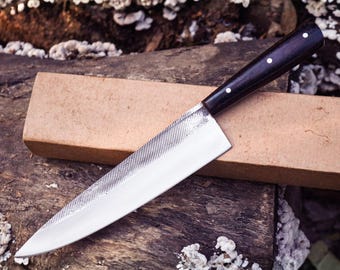 May include: A fixed-blade knife featuring a polished silver-colored metal blade with a textured upper spine and a dark brown wooden handle secured by three small circular rivets. The knife is positioned diagonally across a rectangular tan box.
