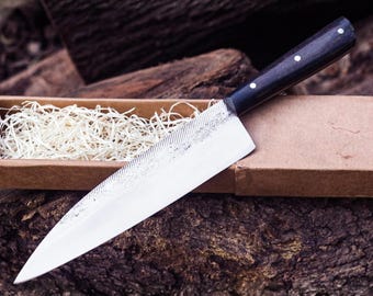 May include: A kitchen knife with a sharp, pointed silver blade featuring a textured finish near the spine and a smooth, polished edge. The handle is made of dark, smooth material and is secured with three small, circular silver rivets.