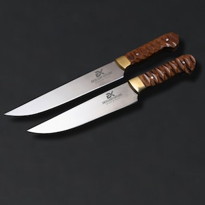 May include: Two knives with silver-toned blades and brown, textured wooden handles. Each blade features a brass-colored bolster and is engraved with the text EXCELLENT CUTLERS. The knives are positioned diagonally, one overlapping the other.