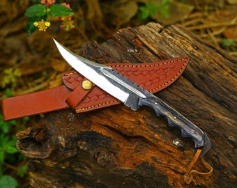 May include: A fixed-blade knife with a polished steel blade featuring a serrated spine, a dark wood handle with brass pins, and a leather sheath with decorative stitching and a brass snap closure, including a small leather lanyard.