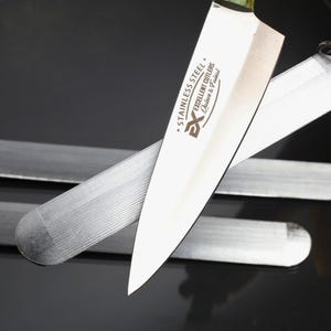 May include: A stainless steel kitchen knife with a pointed blade and the text "STAINLESS STEEL EXCELLENT CUTLERS Quicker & Fastest" printed on the side, positioned over three flat, rectangular metal sharpening stones with attached metal rings.