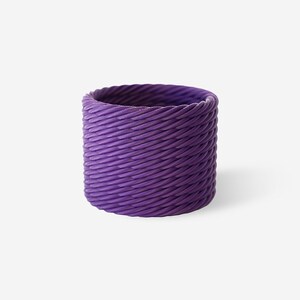 Puede incluir: Un anillo cilíndrico de color morado intenso con una textura continua en forma de cuerda diagonal que envuelve toda la superficie exterior. El objeto tiene una altura uniforme y un patrón consistente y repetitivo de crestas inclinadas.