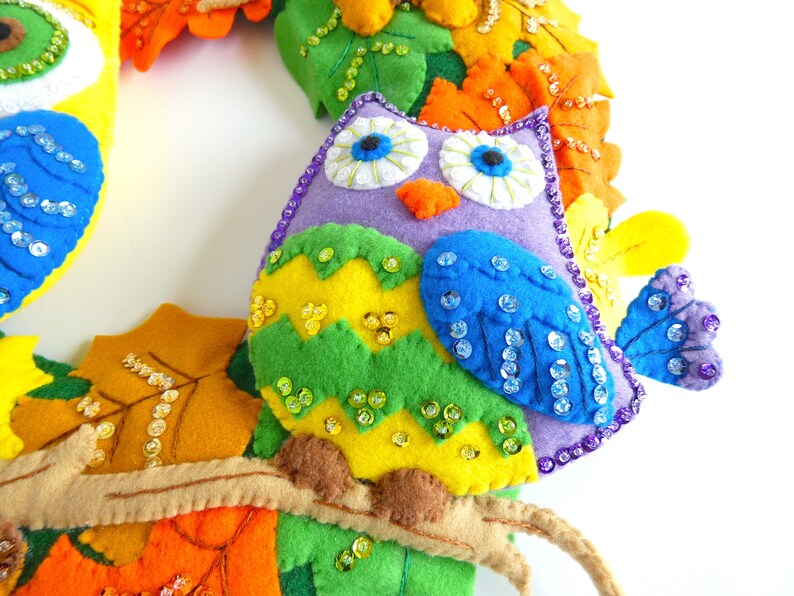 May include: A purple felt owl with green, yellow, and blue felt accents. The owl is decorated with iridescent sequins and has a felt branch attached to its body.