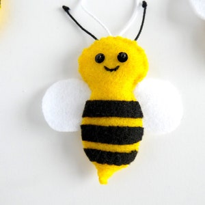 May include: A yellow felt bee with black stripes and white wings. The bee has black eyes and a smiling mouth.