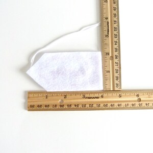 May include: A white felt tie with a string attached. The tie is measured with a ruler, showing it is approximately 4 inches long.