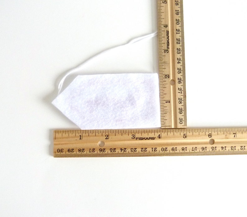 May include: A white felt tie with a string attached. The tie is measured with a ruler, showing it is approximately 4 inches long.