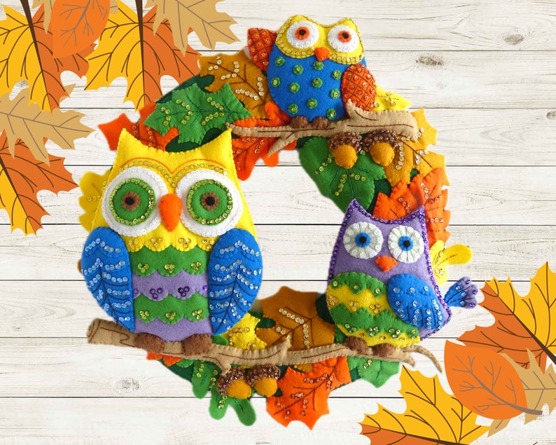 May include: A colorful felt owl wreath with three owls, one yellow, one purple, and one blue, decorated with fall leaves and beads.