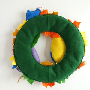 May include: A green felt wreath with colorful felt leaves. The leaves are in shades of yellow, orange, red, purple, and blue.