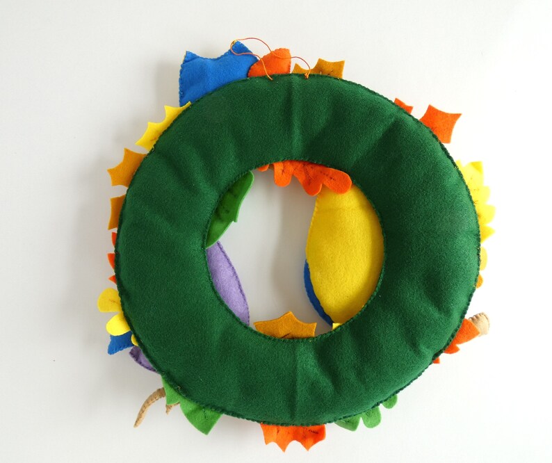 May include: A green felt wreath with colorful felt leaves. The leaves are in shades of yellow, orange, red, purple, and blue.
