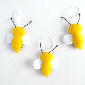 May include: Three felt bee decorations with yellow bodies, black antennae, and white wings. The bees are hanging from white strings.