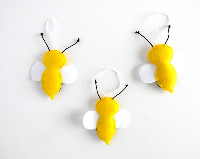 May include: Three felt bee decorations with yellow bodies, black antennae, and white wings. The bees are hanging from white strings.
