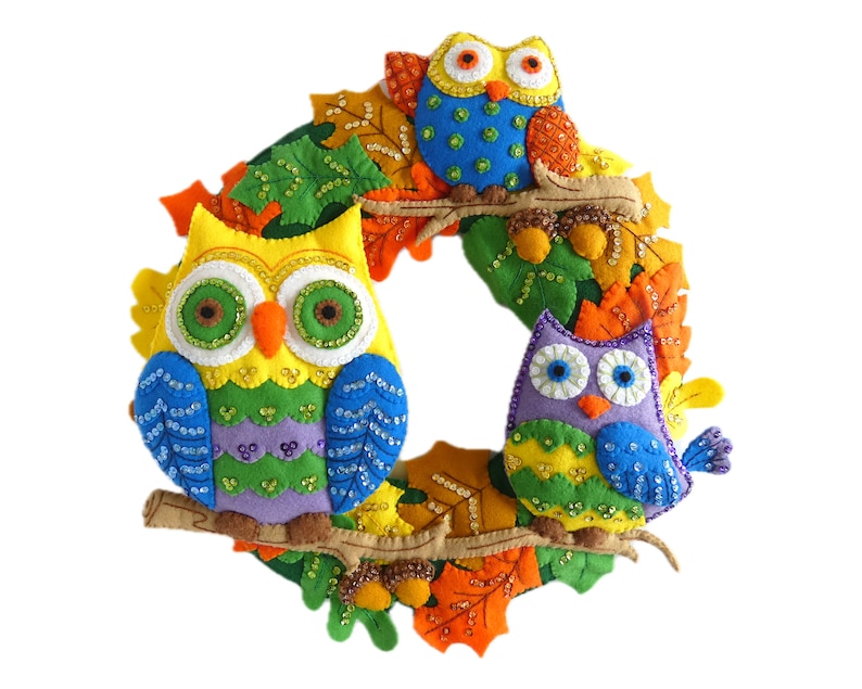 May include: A colorful felt wreath with three owls decorated with sequins. The owls are yellow, green, purple, and blue. The wreath is decorated with felt leaves in shades of orange, green, and yellow.