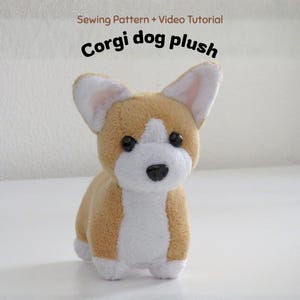 Op de afbeelding: Een pluche Corgi-hondje met beige en witte vacht, zwarte plastic ogen en een zwarte neus. De tekst boven het pluche dier luidt: Sewing Pattern + Video Tutorial, Corgi dog plush. Het speelgoed heeft rechtopstaande oren en een zachte textuur.
