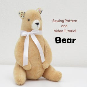 May include: A tan plush bear with a white muzzle, black eyes, and a white satin ribbon tied around its neck. The inner ears feature a multi-colored polka dot pattern. Text reads: Sewing Pattern and Video Tutorial Bear.
