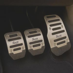 May include: A set of three silver-toned metal car pedals featuring black rubber grip inserts and the text "Sports PEBAL" printed on each. The pedals are secured with visible screws and have a textured, non-slip surface design for vehicle footwells.