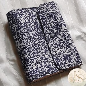 Peut inclure: Un étui rectangulaire en tissu présentant un motif abstrait tacheté bleu marine foncé et blanc. L'étui possède un rabat repliable fixé par un bouton-pression circulaire gris foncé. Le tissu a une texture visible et un aspect plat et structuré.