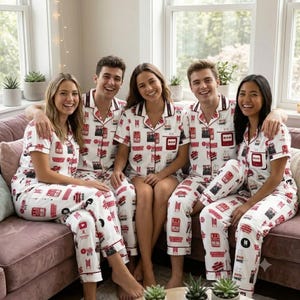 May include: Four individuals wearing matching white pajama sets featuring a repeating red graphic print of various icons and the text BTS. The pajamas consist of short-sleeved button-down shirts with collars and matching long pants with a straight-leg fit.