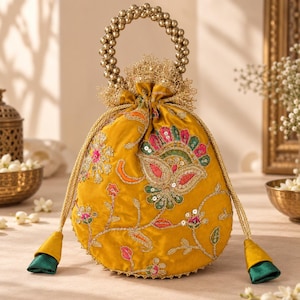May include: A mustard yellow drawstring pouch bag featuring intricate floral embroidery with sequins and beads. The bag has a circular handle made of gold-toned beads and two long drawstrings with green and yellow fabric tassels at the ends.