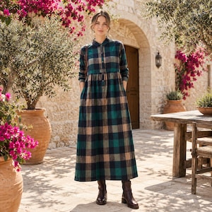May include: A long-sleeved, ankle-length dress featuring a plaid pattern in shades of dark green, navy blue, and beige. The garment has a button-down front placket, a classic collar, and a gathered waistline that flows into a full, loose skirt.