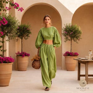 May include: A two-piece set consisting of a cropped long-sleeve top with voluminous sleeves and matching high-waisted wide-leg trousers in a solid light green color. The outfit is worn with black sandals and a woven straw basket bag.
