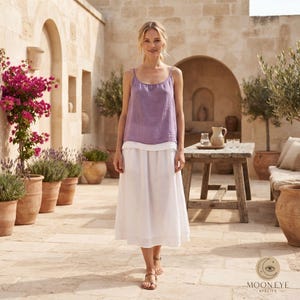 May include: A lavender sleeveless top with a scoop neckline and a white midi skirt. The top features a textured fabric, while the skirt has a layered hemline. The outfit is worn with simple brown sandals, creating a coordinated two-piece ensemble.