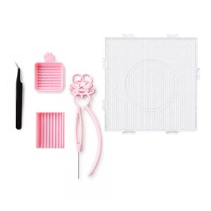 May include: A diamond painting tool kit including a black pair of tweezers, a small pink square tray with a paw print, a pink rectangular grooved tray, a pink stylus with a star and wing design, and a large clear square pegboard with a circle.