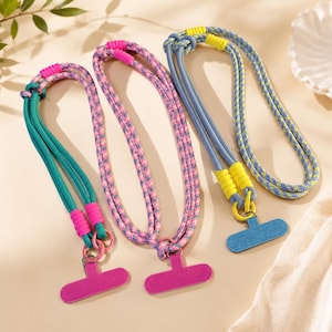 May include: Three phone lanyards featuring braided rope cords in teal, pink, and blue-yellow patterns. Each lanyard includes bright neon-colored cord wraps and a flat, T-shaped connector piece at the bottom for attaching to a mobile device.