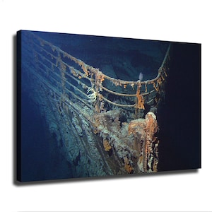 May include: A canvas print featuring an underwater view of the rusted, decaying bow of the Titanic shipwreck. The metal railings are covered in orange and brown corrosion, set against the deep blue, dark abyss of the ocean floor.