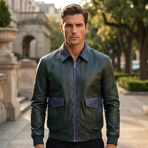 May include: A dark green leather bomber jacket featuring a blue snakeskin-textured collar, a central vertical panel, and two flap pockets. The jacket has a full-length front zipper, ribbed cuffs, and a ribbed hem, providing a structured fit.