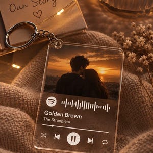 May include: A clear acrylic square keyring featuring a printed photograph of a couple at sunset. The design includes a Spotify-style music player interface with the song title Golden Brown by The Stranglers, a progress bar, and playback icons.