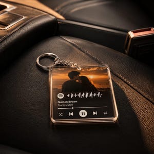 May include: A square clear acrylic keyring featuring a printed photograph of a couple at sunset, a Spotify-style waveform, and the text Golden Brown by The Stranglers, complete with playback control icons and a silver metal split ring attachment.