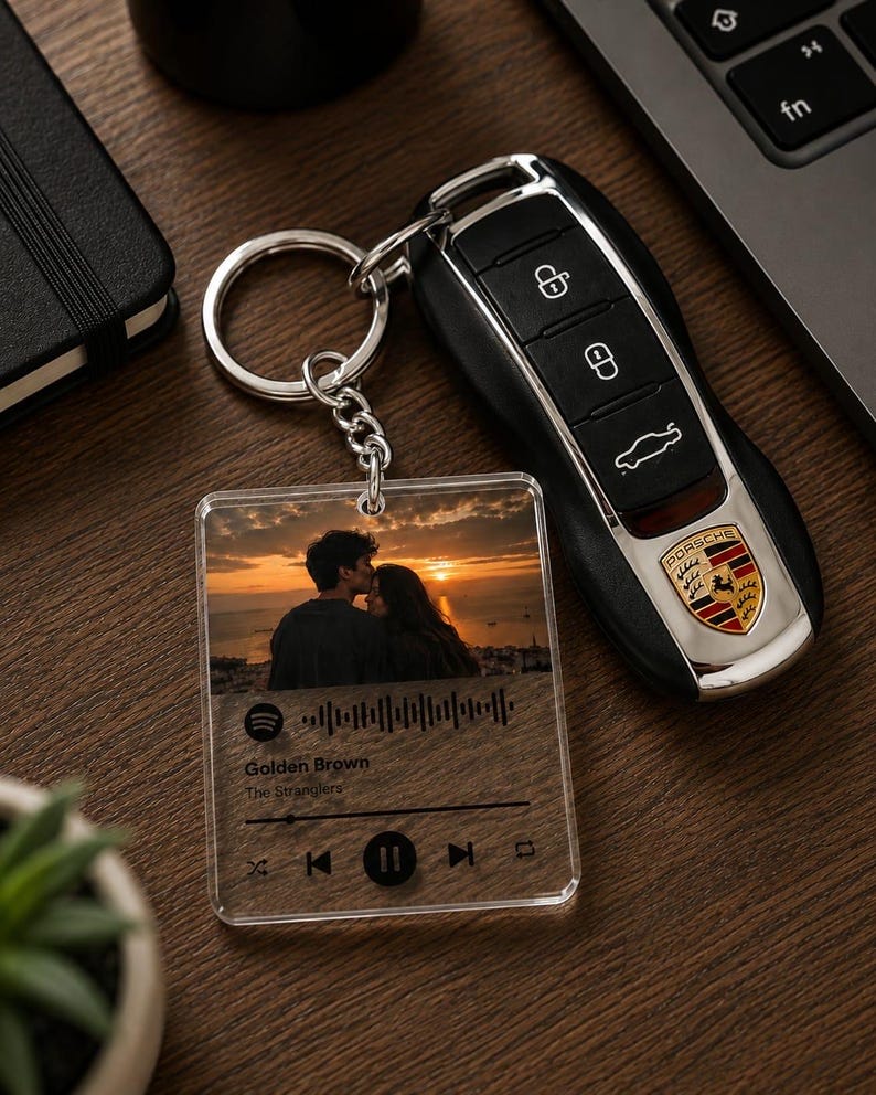 May include: A clear acrylic square keyring featuring a printed photograph of a couple at sunset, a Spotify-style waveform, and the text Golden Brown by The Stranglers, attached to a silver metal ring next to a black Porsche car key fob.