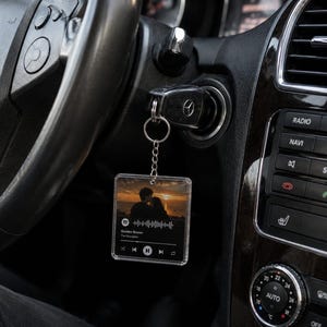 May include: A square, clear acrylic keyring hanging from a car ignition key. The keyring features a printed image of a couple at sunset, a Spotify-style waveform, and the text Golden Brown by The Stranglers with playback control icons.