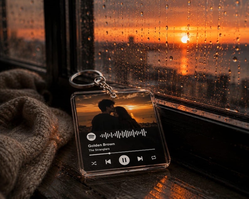 May include: A square clear acrylic keyring featuring a printed music player interface. The design displays a sunset silhouette of a couple, a Spotify code, and the text Golden Brown by The Stranglers with standard playback control icons.