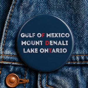 Puede incluir: Un botón circular de color azul marino con texto blanco que dice GULF OF MEXICO, MOUNT DENALI y LAKE ONTARIO. Las letras F, D y T están resaltadas en rojo, creando una secuencia vertical en el centro del botón.