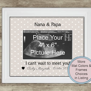 May include: A white picture frame containing a beige mat with white polka dots. The mat features the text Nana & Papa, I can't wait to meet you, Baby Mrozinski, and October 20XX. A placeholder for a 4 inch by 6 inch photo is in the center.