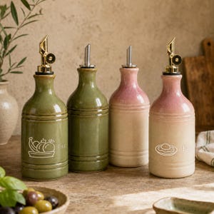 Peut inclure: Quatre distributeurs d'huile en céramique avec des becs verseurs en métal doré. Deux bouteilles sont vert olive, une présente un dégradé de rose et crème, et une autre un dégradé de rose et beige. La bouteille verte porte le texte Fruit.