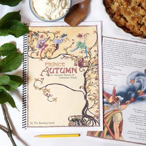 Può includere: Un libro rilegato a spirale intitolato Prince Autumn: An Autumn Nature & Literature Study di The Reading Guild, con un'illustrazione di figure su un albero, accanto a una pagina stampata con testo e un'illustrazione colorata di una figura che soffia foglie.