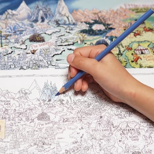 May include: A blue colored pencil held over a black and white line art map of a fantasy landscape. The map features detailed illustrations of mountains, forests, and structures labeled with text including Tumnus's Cave and The Witch's Castle.