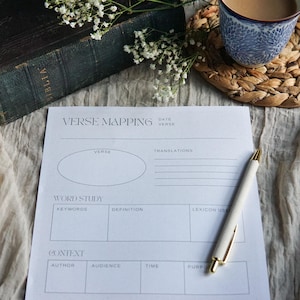 May include: A white paper verse mapping worksheet with black printed text including sections for verse, translations, word study, and context. The sheet features an oval space for verse and grid boxes for study notes, accompanied by a white ballpoint pen.