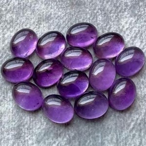 Könnte beinhalten: Eine Ansammlung von zwölf glatten, oval geformten Amethyst-Edelsteinen. Jeder Stein weist eine polierte, glänzende Oberfläche mit tiefvioletten Farbtönen und durchscheinenden Eigenschaften auf, die in einer Gruppe angeordnet sind, um ihre Farbe zu betonen.