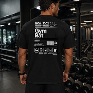 Pode incluir: Uma t-shirt preta de manga curta com texto e gráficos brancos nas costas. O design imita um rótulo nutricional com as palavras Gym Rat, 100% Natural, 100% Protein, um código de barras e ícones que representam força e equipamento de ginásio.