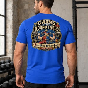 Puede incluir: Una camiseta azul real con un gráfico estampado en la espalda. El diseño muestra a un bufón levantando una barra de pesas con el texto "GAINS OF THE ROUND TABLE", "Thou Shalt Bench in Peace" y "No Jest. Only Chest." El gráfico incluye detalles rojos.