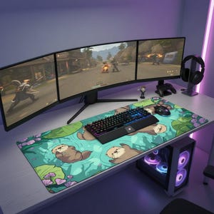 Op de afbeelding: Een grote rechthoekige bureaumat met een herhalend patroon van bruine otters die zwemmen in turquoise water met groene waterleliebladeren en roze bloemen. De mat ligt op een bureau met een mechanisch toetsenbord, gamingmuis, drie monitoren en een headset.