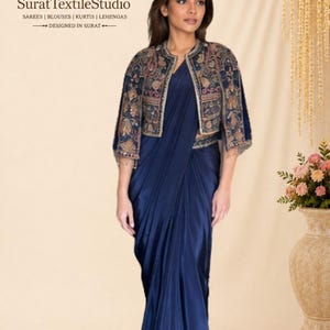 May include: A deep navy blue satin saree paired with a cropped, open-front jacket featuring intricate multi-coloured floral embroidery. The ensemble includes a solid-coloured, floor-length draped skirt and a matching jacket with three-quarter sleeves.